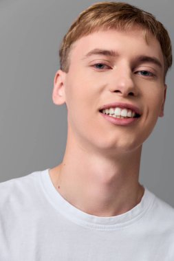 Stüdyo aydınlatmasında günlük beyaz tişört giyen gülümseyen genç adam, yakın çekim neşeli ruh halini vurgulayan, moda, sağlık ve reklam projeleri için çok yönlü