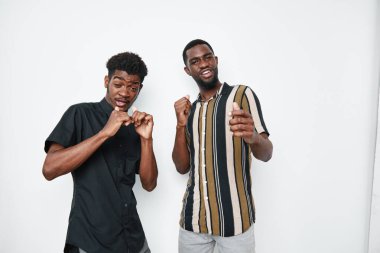 Siyah ve çizgili tişörtlerle gülümseyen ve dans eden koyu tenli genç Afro-Amerikalı erkekler. Arkadaşlık, eğlence ve mutluluk beyaz duvarlı stüdyoda yakalanır..