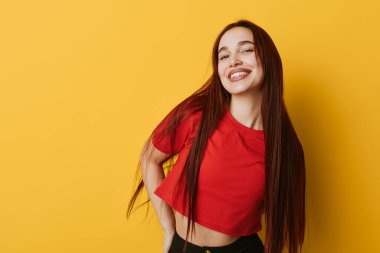 Sarı arka planda kırmızı bluzlu, uzun düz saçlı, gülümseyen kız. Pozitif ruh hali, günlük kıyafet ve gençlik kültürü konsepti için rahat poz..