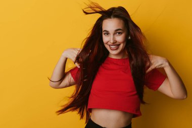 Sarı arka planda duran kırmızı saçlı neşeli genç kadın portresi. Pozitif ifade, günlük kıyafetler, ve kendine güvenen pozlar..