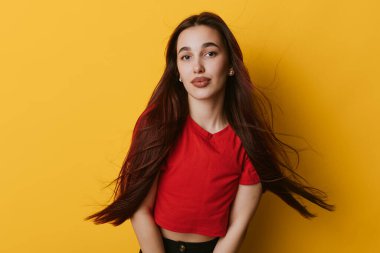 Sarı duvarın önünde kırmızı saçlı dalgalı genç bir kadın portresi, sakin bir yüz ve parlak bir iç mekan tarzıyla öne bakıyor..