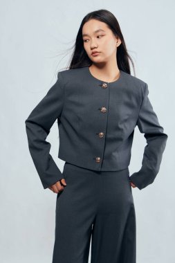 Gri ceketli ve pantolonlu kadın modeli. Profesyonel görünüş ve modern kıyafetler için ciddi bir ifadeyle kalçaları üzerinde duruyor..