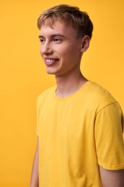 Tek renkli bir ortamda sarı gömlek giyen genç erkek manken, basit kompozisyon, modern gündelik görünüş, doğal poz, stüdyo ışıklandırması sıcaklık ve yakınlık yaratır.