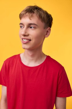 Gündelik gençlik, parlak sarı bir arkaplan önünde kırmızı bir gömlek giyer, modern yaşam tarzını, canlı rengi, kendine güvenen duruşu, moda fotoğrafçılığı için stüdyo düzenini aktarır.