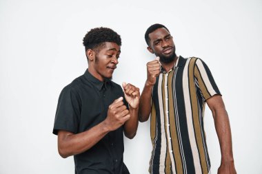 Siyah tenli ve beyaz arka planda günlük gömleklerle gülümseyen Afro-Amerikalı erkekler. Genç arkadaşlar, neşeli ifadeler ve rahat atmosferli müzik ve hareketin keyfini çıkarıyorlar..