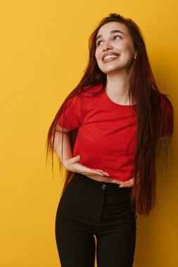 Kırmızı bluzlu, uzun saçlı ve sarı arka planda duran siyah pantolonlu gülümseyen kadın. Neşeli kadın bakışları pozitif ifade ve rahat moda ve yaşam tarzı için başka yöne bakıyor..
