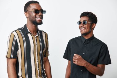 Siyah tenli, güneş gözlüklü Afro-Amerikalı erkekler gülüp eğleniyorlar. Beyaz arka planda günlük giysiler ve arkadaşlık ve yaşam tarzı için mutlu ifadeler..