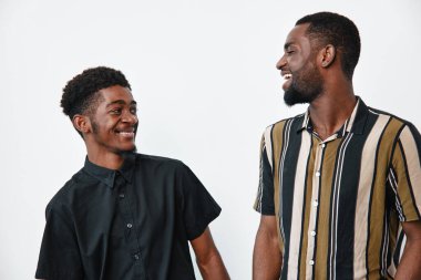 Siyah çizgili ve siyah tişörtlü Afro-Amerikalı erkekler beyaz arka planda gülümsüyor ve etkileşime giriyorlar. Genç siyah erkekler içeride dostluk ve neşe gösteriyorlar..