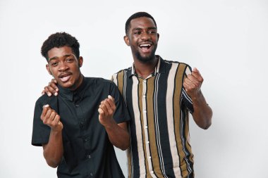 Siyah tenli, sıradan tişörtlü, gülümseyen ve heyecan gösteren Afro-Amerikalı erkekler. Arkadaşlık, kutlama, mutluluk ve beyaz stüdyo arka planında pozitif ruh hali.