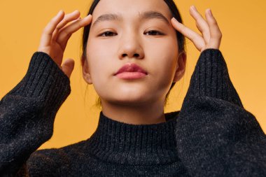 Siyah örülü süveter giyen kadın, elleri ılık sarı arka planda olan saçları ayarlıyor. Pürüzsüz tenli ve kendine güvenen kadın modelin yakın portresi yaşam tarzı ya da tarzı arıyor..