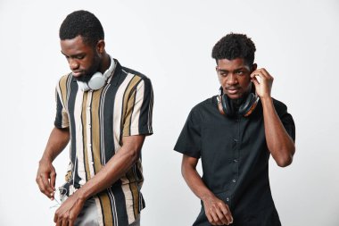Siyah tenli, kulaklıkla poz veren genç Afro-Amerikan erkekler. Biri çizgili gömlek, diğeri siyah gömlek giyiyor. İkisi de beyaz arka planda gündelik tarz ve modern modayı gösteriyor..