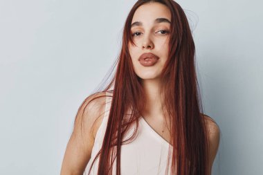 Düz kızıl saçlı ve minimum makyajlı genç bir kadın portresi düz ışık duvarının önünde kolsuz bluz giyerek duruyor. Rahat duruşu ve doğal görünüşü olan bir kadın model..