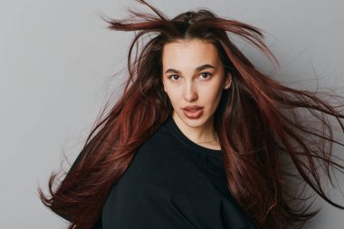 Kahverengi saçlı genç kadın hareket halinde, doğrudan kameraya bakıyor. Etkileyici gözleri ve tarafsız arkaplanda siyah giysisi olan çekici bir kadının stüdyo portresi..