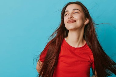 Gülümseyen kadın, uzun saçlı, kırmızı bluzlu, mavi arka planda. Rahatlamış yüzü ve stüdyo ortamında çekilmiş olumlu duyguları olan genç bir kadının yakın plan portresi..