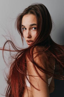 Kızıl saçlı, çıplak omuzlu ve yoğun bakışlı genç bir kadının portresi. Yumuşak doğal ışık, minimalist stüdyo ortamında deri dokusunu ve saç tellerini ön plana çıkarıyor.