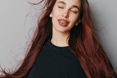 Gülümseyen kızın portresi, dalgalı kızıl saçlar ve kapalı gözler, siyah gömleğin içinde dili dışarı çıkmış. Genç, neşeli ve rahat, doğal makyajlı ve küpe takan bir kadın..