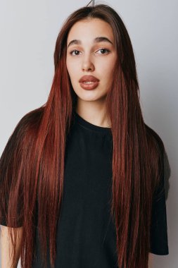 Uzun kahverengi saçlı ve siyah gömlekli genç bir kadın beyaz duvarın önünde poz veriyor. Moda, tarz ya da yaşam tarzı fotoğrafçılığı için ciddi bir yüzü var..