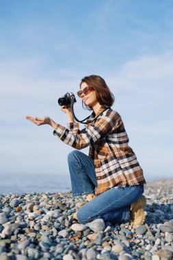 Açık hava çekimi, rüzgarlı bir sahilde kameralı bir kadın yakalar, rahat bir şekilde, doğal ışık, deniz manzarası ve kayalıklarda canlı bir yaşam tarzı için..