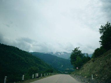 Alp manzarası, sisli bulutlar, yeşil yamaçlar ve korkuluklar arasında dolambaçlı otoban, doğa, manzara ve yol gezisi ve macera fotoğrafçılığı için ideal bir açık yol rotası.