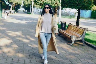 Moda, kadın, palto, sokak, park, yürüyüş, açık hava, tarz, gündelik, güneş ışığı, güneş gözlüğü, güneşli bir park caddesinde zarif bir yürüyüş bej bir ceket ve kot pantolonla şık bir konfor ve rahatlık içinde