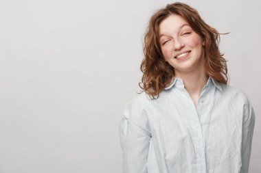 Dalgalı saçlı, beyaz düğmeli gömlek giyen genç bir kadın. Hafif nötr arka plan, basit bir portre konseptinde doğal güzelliği ve sıradan modayı ön plana çıkarıyor..