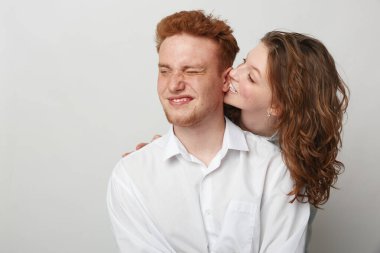 Gündelik beyaz gömlekli mutlu genç çift, sevgi dolu bir anı paylaşıyor, kadın erkeği yanağından öpüyor. Tarafsız bir geçmişe sahip stüdyo ayarları, aşk, neşe ve yakın ilişki kavramı.