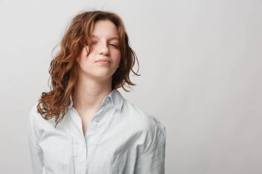 Beyaz tişörtlü, kıvırcık saçlı, kendine güvenen ve rahat bir ifadeyle arka planda duran genç bir kadının portresi. Doğal güzellik kavramı, gündelik moda ve kendine güven..