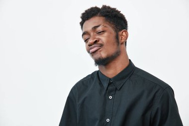 Siyah tenli, beyaz arka planda siyah gömlekli kendinden emin genç bir adam. Kısa kıvırcık saçlı Afrikalı etnik erkek. Davranış ve günlük moda..