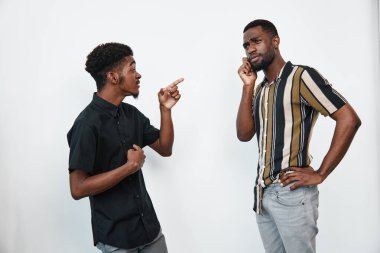 Esmer tenli Afro-Amerikalı erkekler yoğun bir tartışma içindeler. Bir adam parmaklarıyla hareket eder, diğeri eli yüzü üzerinde durur, ikisi de beyaz arka plana karşı günlük gömlekler giyer..