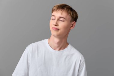 Markasız bir moda havası, beyaz tişörtlü gülümseyen genç bir adam, sakin duruş, minimal fon ve yaklaşılabilir ruh hali..