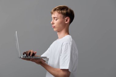 Genç adam iş için dizüstü bilgisayar kullanıyor, klavyede sakin bir ifade, minimum stüdyo arkaplanı, teknoloji yaşam tarzı, çevrimiçi görevler ve temiz bir çağdaş ortamda üretkenlik ile daktilo kullanıyor.