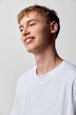 Beyaz tişörtlü, gülümseyen bir adamla parlak bir stüdyo ayarı. Neşeli bir gençlik enerjisi yayıyor. Pazarlama ve editör içeriği için doğal bir kolaylık.