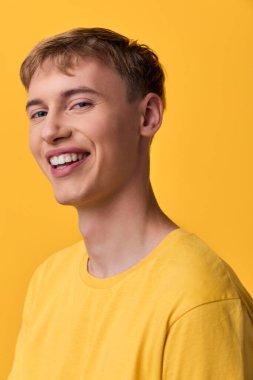 Sarı tişörtlü neşeli bir adam cesur bir stüdyo arka planında gülümsüyor. Markalaşma, yaşam tarzı ve stok fotoğrafçılığında pozitif iletişim için ideal.