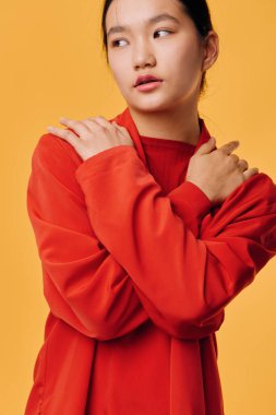 Kırmızı kazaklı genç Asyalı bir kadının portresi. Kollarını kavuşturup başka tarafa bakıyor. Minimalist stüdyo, sıcacık renklerle ve güzellik ve sağlık teması için günlük kıyafetlerle çekilmiştir..