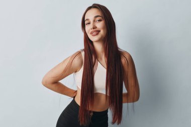 Uzun saçlı, kendine güvenen bir manken elleri belinde sıradan beyaz kolsuz bir bluz ve siyah taytlar giyiyor..