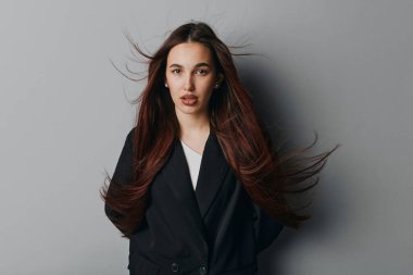 Gri arka planda siyah ceket giyen uzun saçlı genç bir kadının portresi. Gevşek saçlı, sakin yüzlü, yumuşak ışıklandırma ve tarafsız arka planla stüdyoda poz veren kadın model..