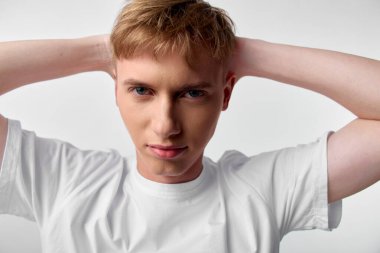 Adam rahat poz verir. Beyaz tişört stüdyosunun arkasında. Kendine güvenen ifadeler yakar.