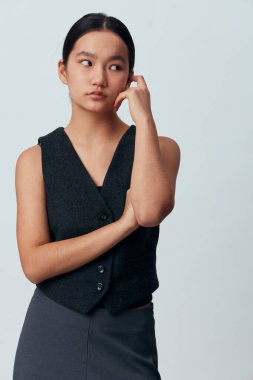 Koyu renk kolsuz yelek ve yüzü yana bakan etekli düşünceli genç bir kadının portresi. Tarafsız arka planda sırtı kıllı Asyalı kadın rahat ve sakin bir hava sergiliyor..