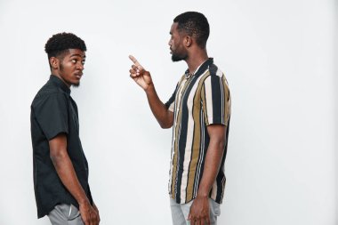 Siyah tenli, sıradan giyinmiş Afro-Amerikalı erkekler önemli bir şeyi tartışıyorlar. Bir adam parmaklarıyla hareket ederken diğeri beyaz arka planda ona bakıyor..