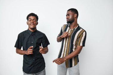 Siyah tenli Afro-Amerikalı erkekler dans ediyor ve beyaz arka planda günlük kıyafetler içinde gülümsüyor. Arkadaşlar müziğin ve dinlenme zamanının keyfini çıkarıyorlar..