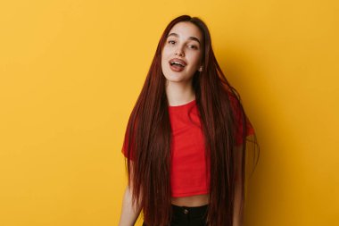 Sarı duvarın önünde duran uzun düz saçlı, gülümseyen genç kadın. Kırmızı gömlek, günlük kıyafet ve rahat poz stüdyoda moda ve güzellik konsepti için..