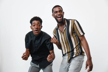 Koyu tenli mutlu siyahi adamlar günlük kıyafetlerle heyecan ve coşku gösteriyorlar. Arkadaşlar gülümsüyor ve hayat tarzı ve arkadaşlık için beyaz arka planda enerjik pozlarla kutluyorlar..