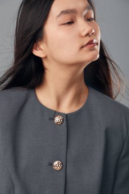 Siyah saçlı, gri ceketli, metalik düğmeleri olan genç bir kadının portresi. Moda ve güzellik konsepti için arka planda kapalı gözlerle yan bakıyor..