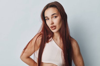 Düz kızıl saçlı, beyaz kolsuz bluzlu, kameraya bakan genç bir kadın. Az makyajlı yakın plan portre, doğal ten rengi ve güzellik konsepti için basit fon..