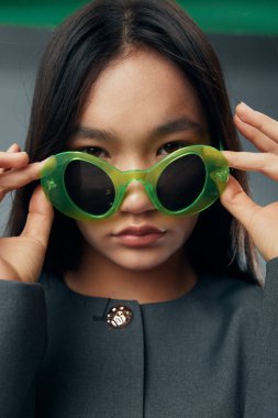 Yüzüne yeşil güneş gözlüğü takan kadın portresi. Doğal görünümlü, minimum makyajlı ve basit stüdyo ortamında benzersiz aksesuarlara odaklan..