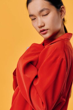 Parlak turuncu arka planda kırmızı kazakla poz veren genç bir kadın. Günlük tarz, moda ve portre fotoğrafı için. Yumuşak ifadeli ve rahat giyimli bir kadın modeli..