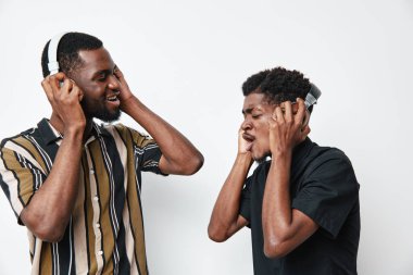 Siyah tenli genç adamlar kulaklıkla müzik dinliyorlar, neşe ve bağlantı belirtiyorlar, parlak stüdyo ortamında beyaz duvarlı günlük gömlekler giyiyorlar..