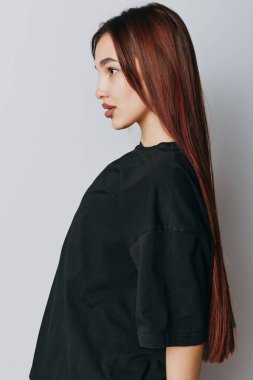 Siyah tişörtlü, açık arkaplanda poz veren uzun saçlı genç bir kadın. Pürüzsüz ciltli bir kadın portresi ve kapalı alanda minimalist bir şekilde rahatlamış bir ifade..