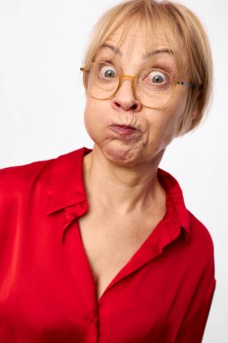 Orta yaşlı, gözlüklü ve kırmızı gömlekli bir kadının şişkin yanaklı ve geniş gözlü komik bir yüz ifadesi. Beyaz arka planda izole edilmiş stüdyo çekimi, neşeli bir ruh hali..