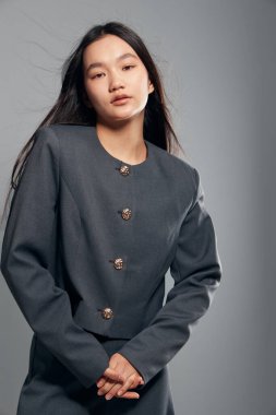 Moda konsepti için modern tarz, saç stili ve profesyonel görünüm sergileyen, arka planda düğmeleri olan gri ceketli genç bir kadın model..